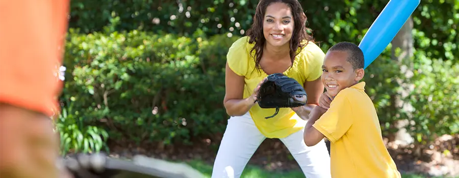 Woman and child smiling and playing baseball outside on a sunny day