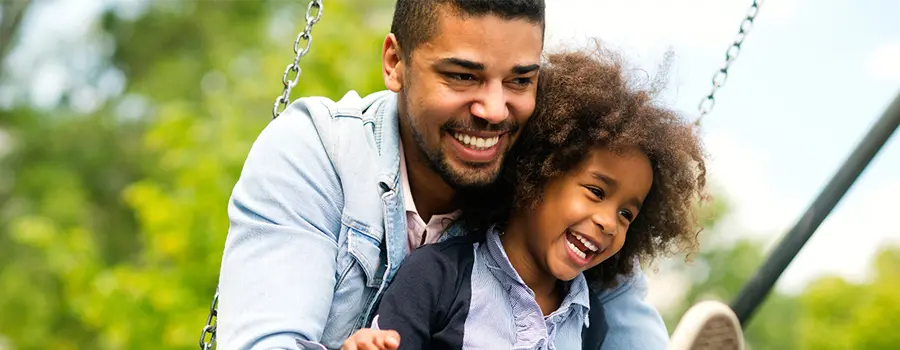 An adult and child smiling and swinging on a swing