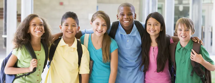 A group of smiling school children wearing backpacks.
